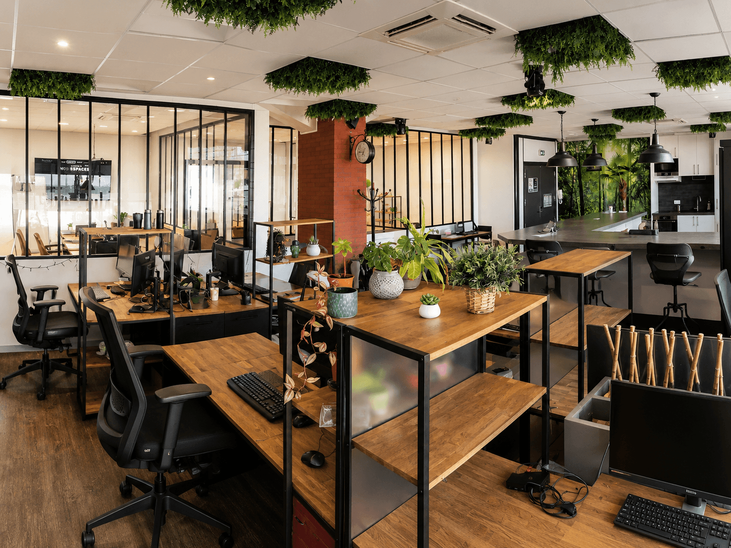 Open space lumineux avec tables en bois, verrières noires et plantes suspendues